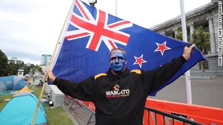 Protestujący trzyma flagę Nowej Zelandii stojącą przed budynkami Parlamentu w czwartym dniu demonstracji przeciwko ograniczeniom Covid-19 w Wellington 11 lutego.