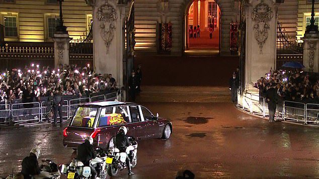Państwowy kondukt pogrzebowy niesie trumnę królowej przez bramy pałacu przy aplauzie tłumu.